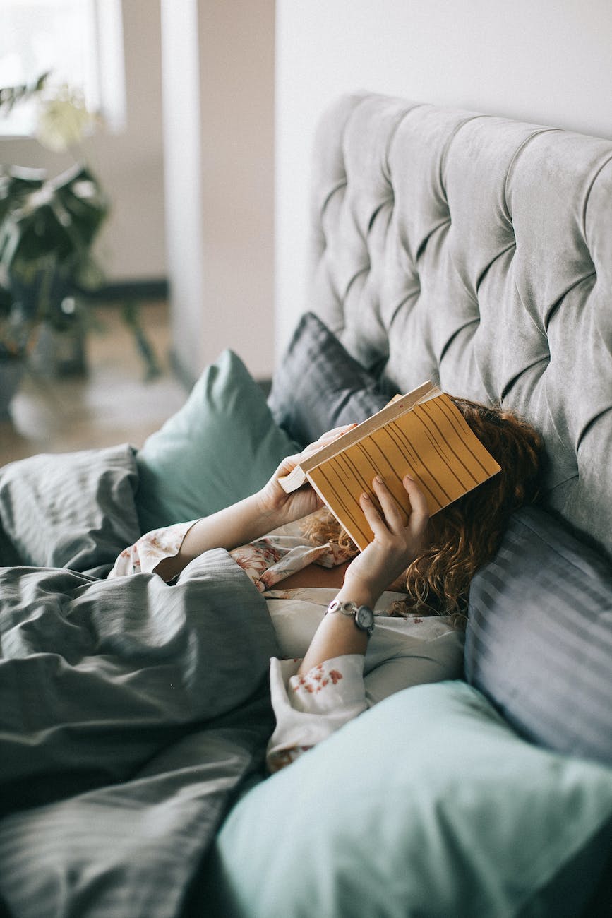 woman covering face with book on bed